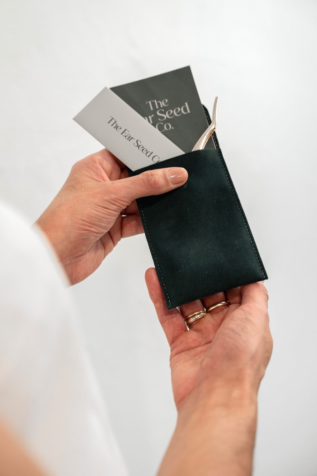A close-up of a person's hands holding a dark green leather seed packet holder, with seed packets tucked into the pocket. The brand name 'The Far Seed Co.